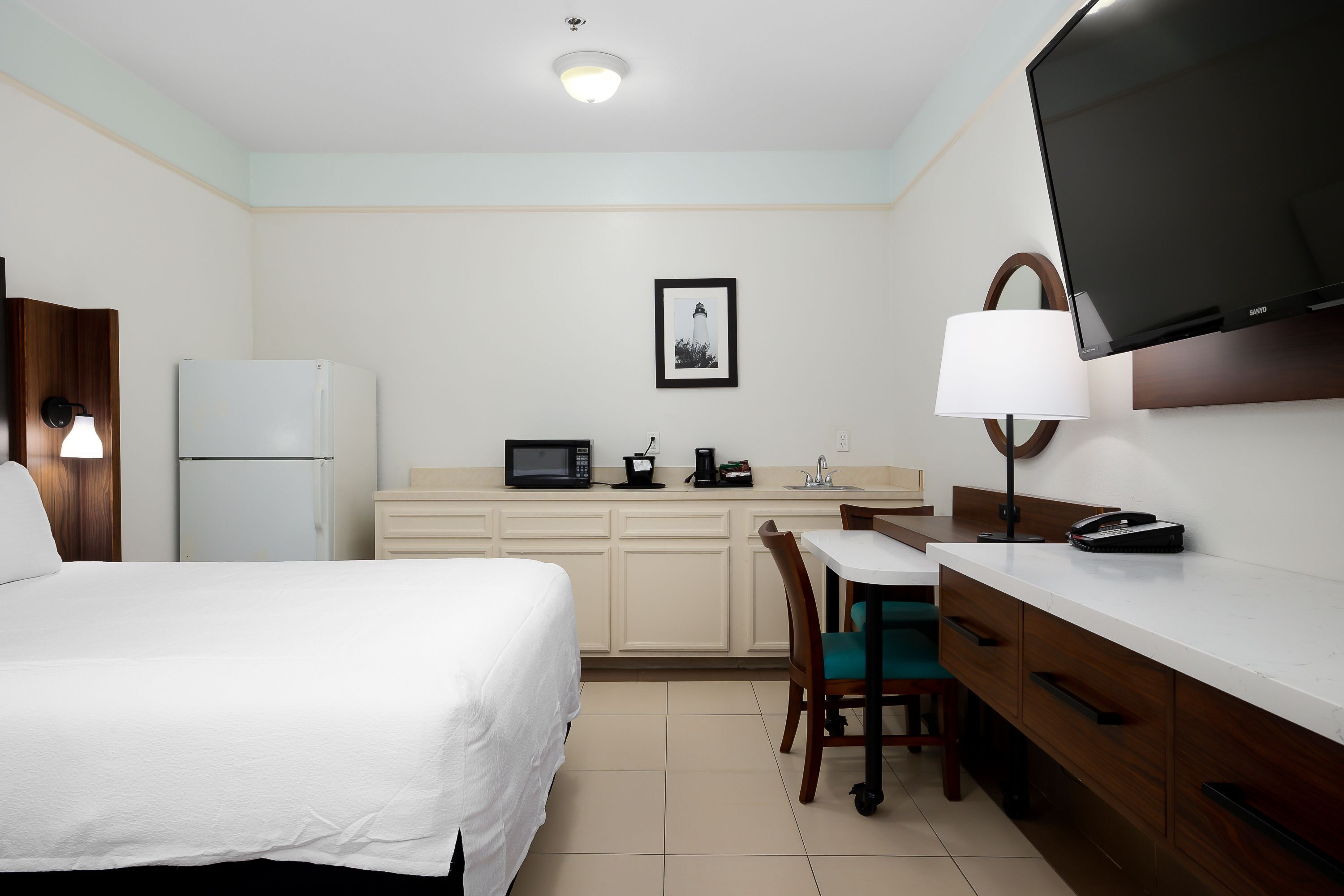 Une chambre d’hôtel équipée d’un lit, d’un bureau, d’un four à micro-ondes, d’un réfrigérateur, d’une télévision et d’un tableau au mur.