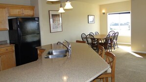 A kitchen with granite countertops, a stainless steel sink, a black refrigerator, wooden cabinets, and pendant lighting.