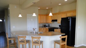 A modern kitchen with a central island, wooden bar stools, a black refrigerator, and wooden cabinets.