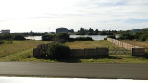 A grassy area with a wooden fence, a road, and a body of water in the background.