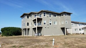 A multi-story residential building with a balcony on the second floor, a small outdoor seating area, and a sign indicating a rental property.