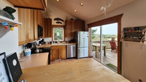 A modern kitchen with wooden cabinets, a stainless steel refrigerator, and a large window overlooking a deck.