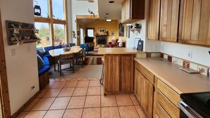 A kitchen with wooden cabinets, a dining area with blue chairs, and a large window.