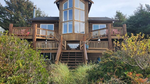 A two-story wooden house with a central glass tower, wooden balconies, and a staircase leading to the upper level.