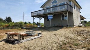 A two-story house with a balcony, a sign advertising beach rentals, and construction materials on the ground.
