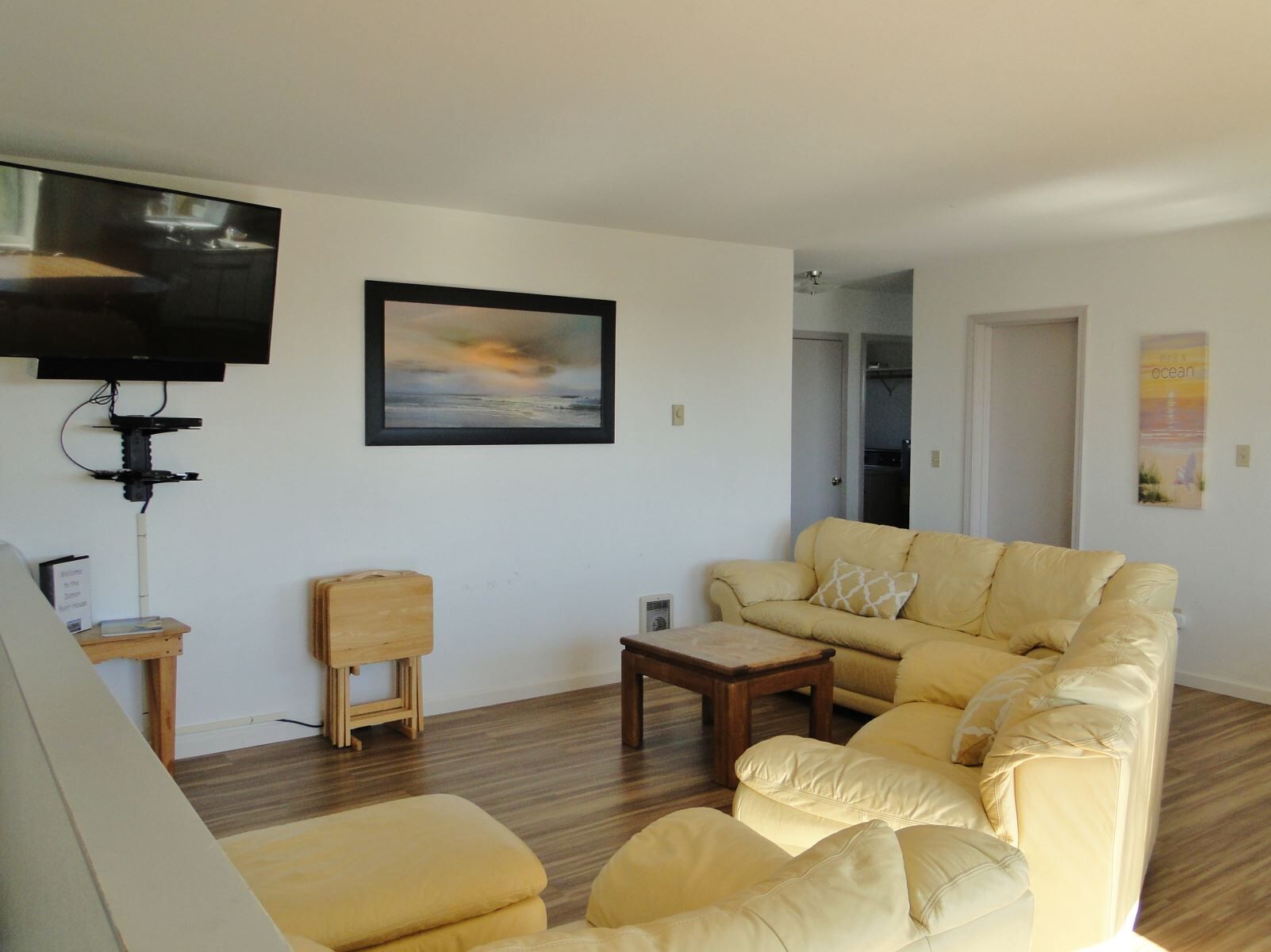 A living room with a beige sofa, a coffee table, a TV mounted on the wall, and a framed picture.