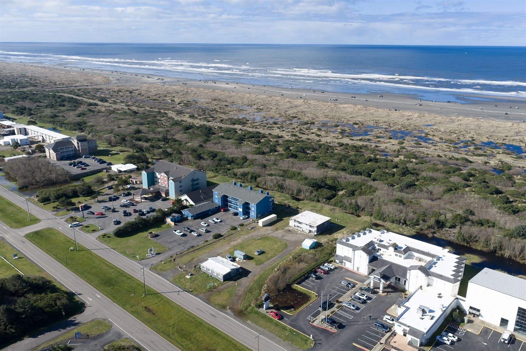 Vue aérienne d’une zone côtière comprenant un parking, des bâtiments et une plage.