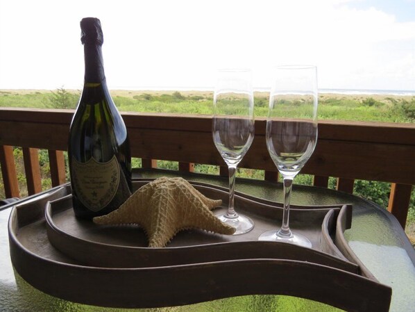 A bottle of wine and two glasses on a table with a starfish decoration, overlooking a grassy landscape.