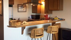 Une cuisine compacte avec des meubles en bois, un four à micro-ondes, une cafetière rouge et un panier de fruits posé sur le plan de travail.