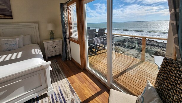 Une chambre dotée d’une grande porte-fenêtre coulissante qui donne sur une terrasse en bois offrant une vue sur la plage.