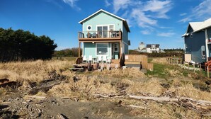 Une maison à deux étages avec un balcon, située dans un espace verdoyant sous un ciel dégagé.