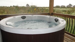 A hot tub on a wooden deck with a view of a grassy field and houses in the background.