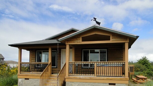 A two-story log cabin with a balcony, a chimney, and a small deck area.