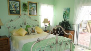 Un dormitorio con cama, mesita de noche, lámpara, ventana con cortinas y vistas a la terraza exterior.