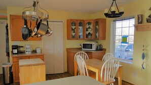 Cocina compacta con armarios de madera, microondas, cafetera y una mesa de comedor con sillas.