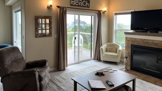 A living room with a brown leather sofa, a white armchair, a coffee table, a fireplace, and a large TV. - Bristol Court C- Beautiful 3 Bedroom (Ocean Shores)