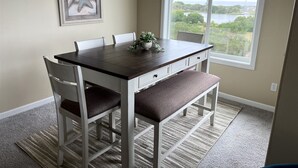 A dining area with a table, chairs, and a view of a lake through a window. - Bristol Court C- Beautiful 3 Bedroom (Ocean Shores)