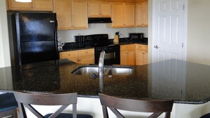 A kitchen with wooden cabinets, a black refrigerator, a stainless steel sink, and a granite countertop. There are three pendant lights hanging above the island. - Bristol Court D- Beautiful 3 Bedroom (Ocean Shores)