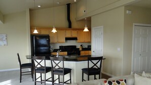 A modern kitchen with wooden cabinets, a black refrigerator, and a dining area with a round table and four chairs. - Bristol Court D- Beautiful 3 Bedroom (Ocean Shores)