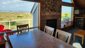 A dining area with a view of the beach, a stone fireplace, and a wooden ceiling.