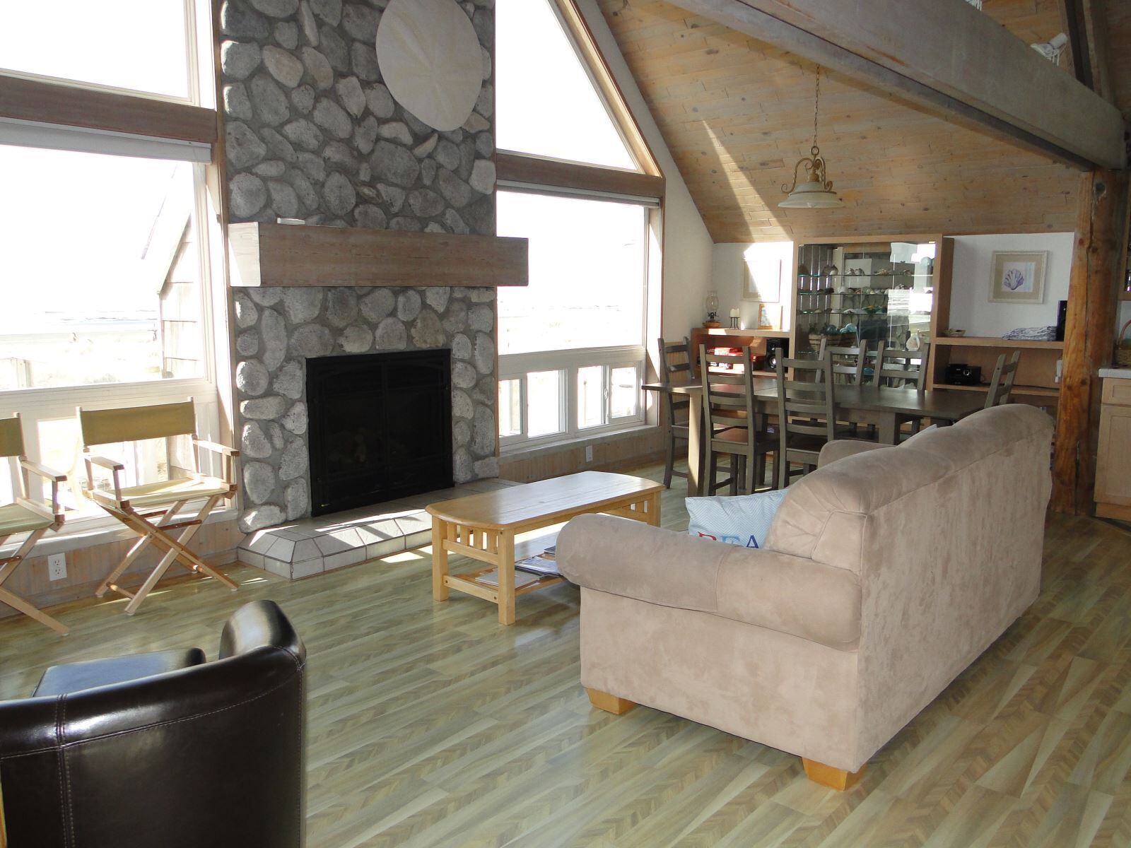 A spacious living room with a stone fireplace, wooden furniture, and large windows.