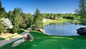 A golf course with a pond, a walking path, and surrounding greenery.