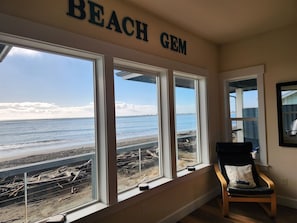 A room with a large window overlooking a beach, a chair, and a sign reading "BEACH GEM".