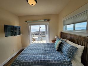 A bedroom with a bed, a TV, a view of the sea, and a window. - Beach Gem- Private Beach - Hot Tub (Ocean Shores)
