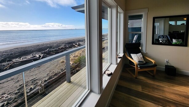 Une pièce dotée d’une grande fenêtre donnant sur une plage, d’une chaise et d’un miroir accroché au mur.