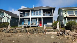 Une maison à deux étages avec un balcon, une porte rouge et un mur de pierre au premier plan.