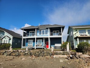 A two-story house with a balcony, a red door, and a stone wall in the foreground.