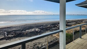 Une vue sur la plage depuis une terrasse couverte avec une balustrade, une plage de sable et des morceaux de bois flotté éparpillés.