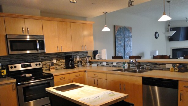 A modern kitchen with stainless steel appliances, wooden cabinets, and a central island with a chalkboard. - Outlook 309/Oyhut Bay (Ocean Shores)