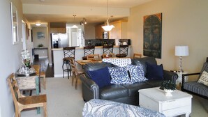 A living room with a sofa, a patterned ottoman, a coffee table, and a dining area with a table and chairs. - Outlook 309/Oyhut Bay (Ocean Shores)