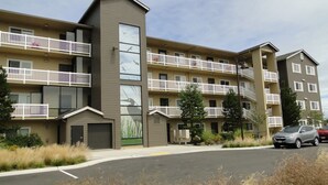 A multi-story apartment building with balconies, a garage, and a landscaped area with dry grass. - Outlook 309/Oyhut Bay (Ocean Shores)