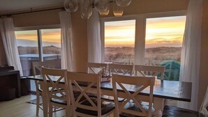 A dining area with a table and chairs, large windows with curtains, and a view of the landscape. - Sea Angel - Stunning views from this ocean front home ! (Moclips)