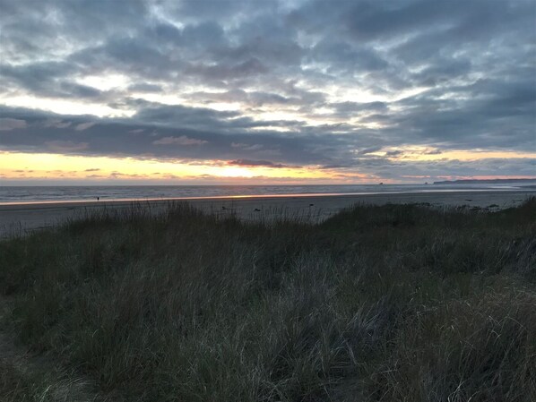 Una playa con cielos nublados y una persona caminando a lo lejos.