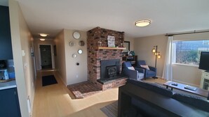 A modern living room with a brick fireplace, a flat-screen TV, and a seating area with blue chairs. - Sea Angel - Stunning views from this ocean front home ! (Moclips)