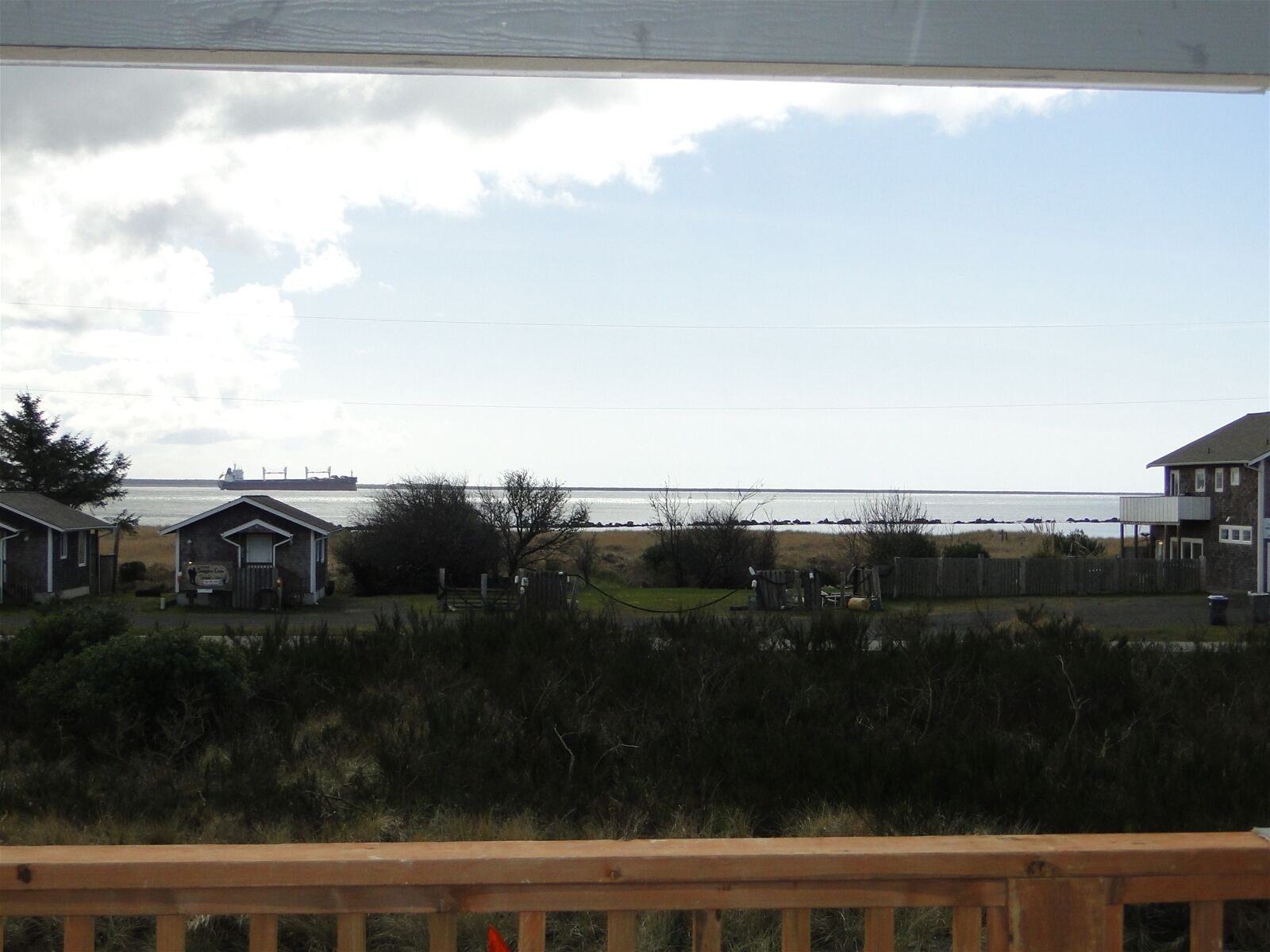 En kustutsikt med ett trädäck, strandhus och ett stort fartyg i fjärran.