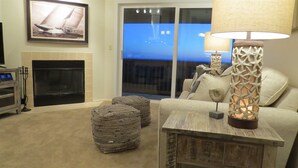A living room with a fireplace, a television, and a view of the ocean through a sliding glass door.