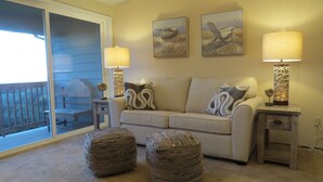 A living room with a sofa, two side tables, two lamps, two woven ottomans, and two wall-mounted paintings.