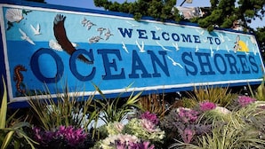 A sign welcoming visitors to Ocean Shores, featuring seagulls, a seahorse, and a sunset.