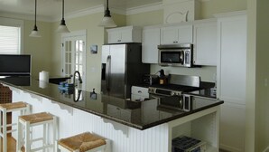 Une cuisine moderne dotée d’un îlot central, de meubles blancs, d’appareils électroménagers en acier inoxydable et de luminaires suspendus.