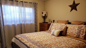 Een slaapkamer met een groot bed, een dressoir, een nachtkastje, een lamp en een sterren decoratie aan de muur.