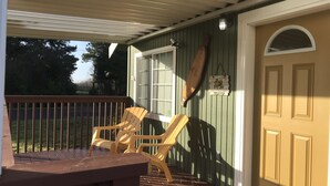 Een houten terras met Adirondack-stoelen en een bank, een deur met raam, en een wandlamp.