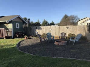 Un jardin avec un foyer, quatre chaises Adirondack, une clôture en bois et un abri de jardin.