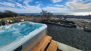Una vasca idromassaggio con un pontile in legno, affacciata su una costa rocciosa con vista sull'oceano e sulla terraferma in lontananza.