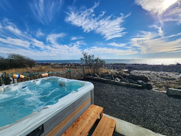 Ein Whirlpool mit einer Holzterrasse, mit Blick auf eine felsige Küste und eine Fernsicht auf das Meer und Land.