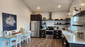 Una cucina moderna con pavimento in legno, pensili e basi bianchi e scuri, elettrodomestici in acciaio inossidabile e un tavolo da pranzo blu con sedie bianche.
