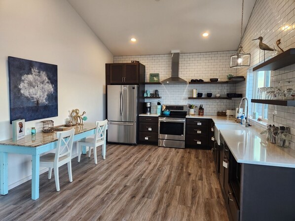 Une cuisine moderne avec un plancher en bois, des meubles de couleur blanche et foncée, des appareils en acier inoxydable et une table à manger bleue avec des chaises blanches.